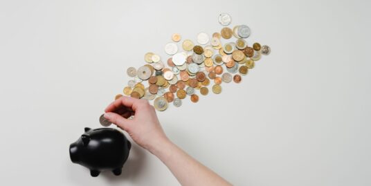 mulher colocando moedas no porquinho para aprender como juntar dinheiro para comprar um imóvel